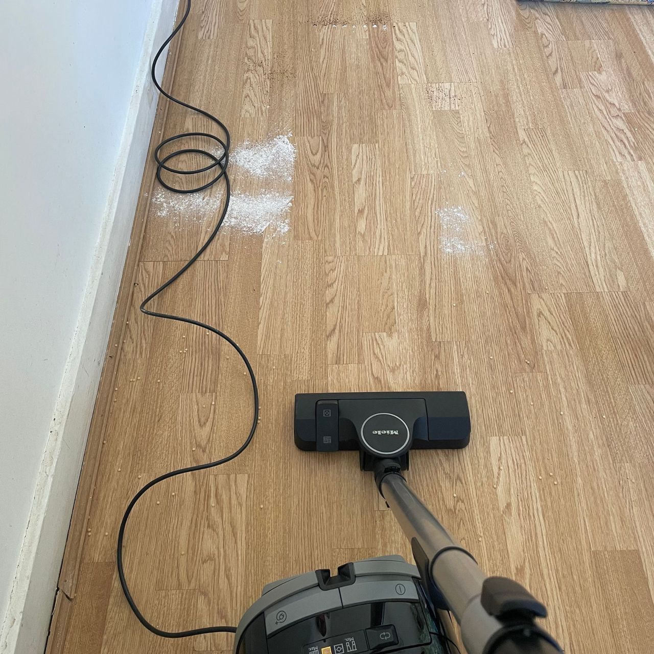 Miele cylinder vacuum on hardwood floor next to cous cous, flour and sugar, and coffee grounds