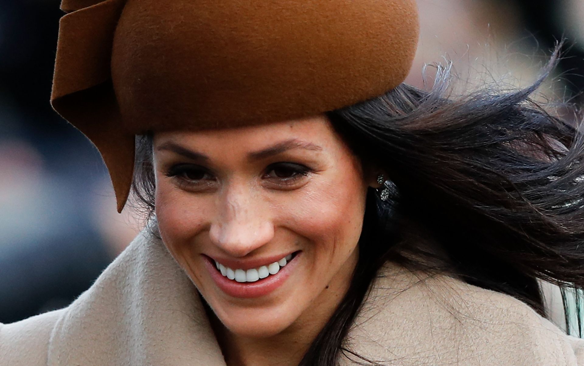 Meghan Markle wearing a brown hat and smiling