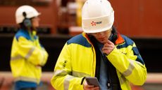An Electricite de France SA (EDF) engineer wearing a high-vis jacket checks a smartphone at the Gravelines nuclear power station, operated by EDF.
