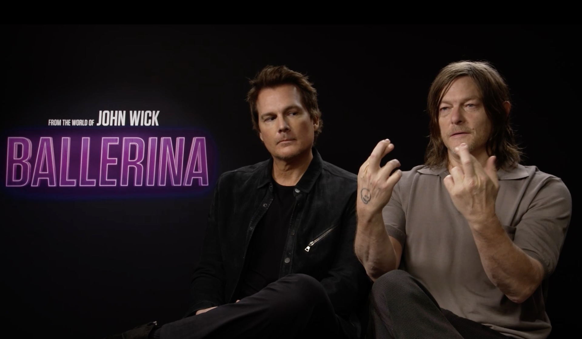 Len Wiseman and Norman Reedus sat being interviewed in front of the Ballerina logo