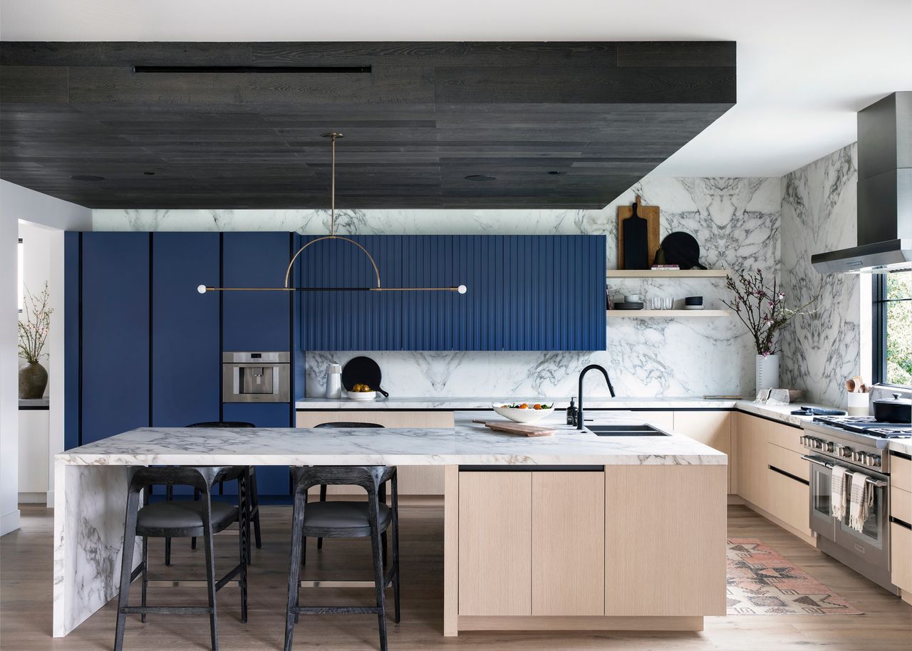 Pale oak kitchen with dark blue back units, white marble countertop and backsplash, and black ceiling feature