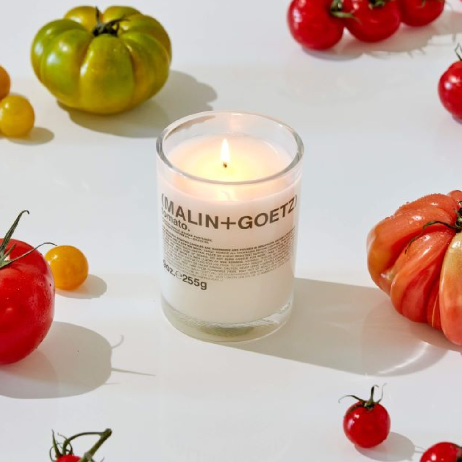 A white glass candle by heirloom tomatoes