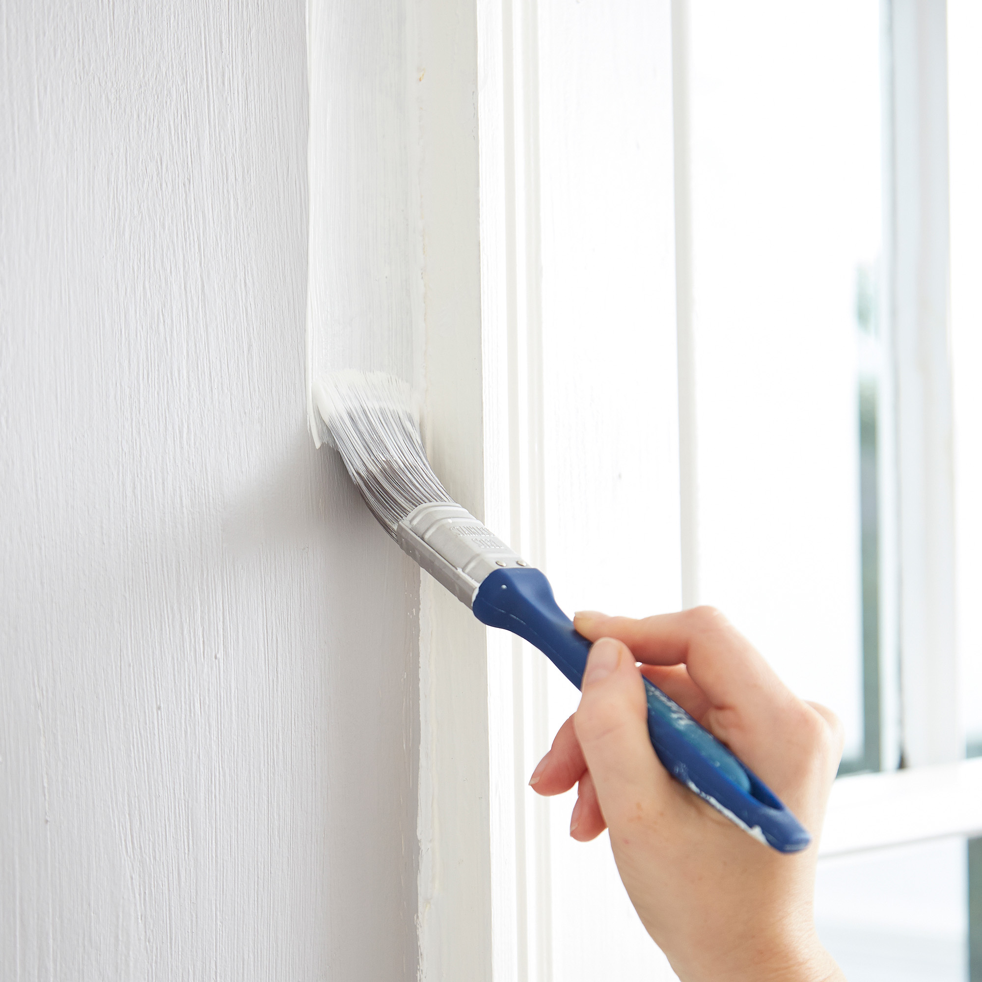 Female painting wall next to window