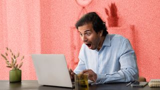 Man looking shocked whilst sitting in front of a laptop.