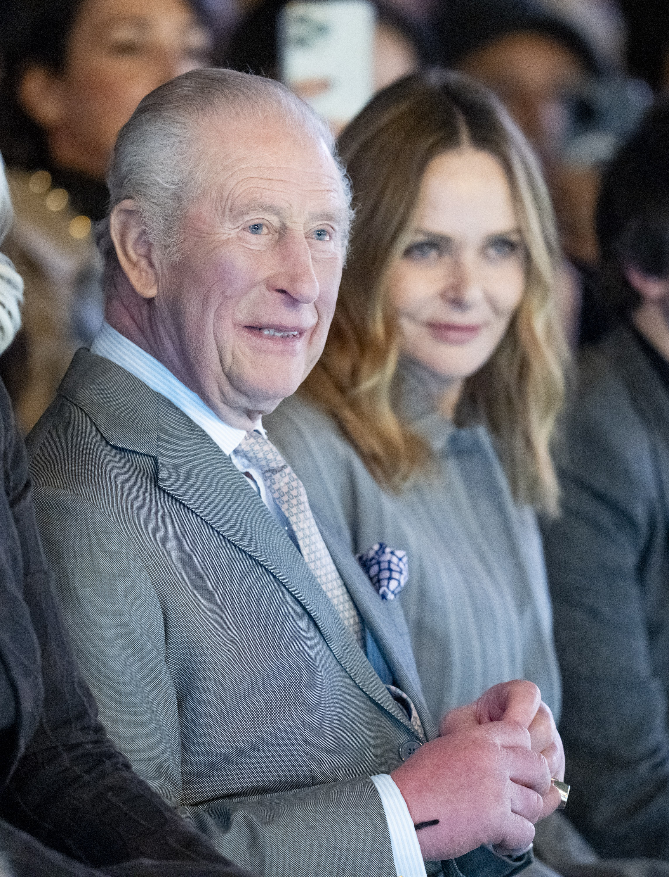 King Charles wearing a gray suit sitting next to Stella McCartney at Fashion Week