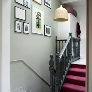 A landing with a built in wardrobe, a gallery of artwork and a rattan light, with a red carpet staircase and black handrail