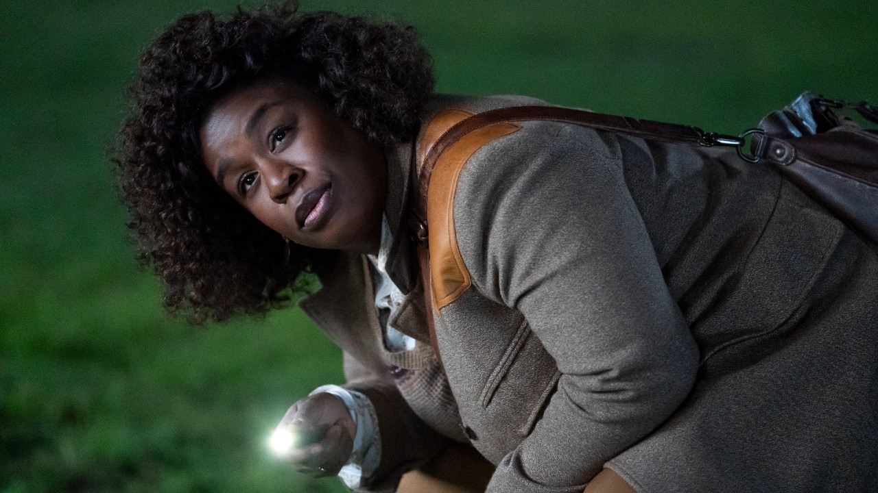 Uzo Aduba leaning down and shining a flashlight with her left hand.