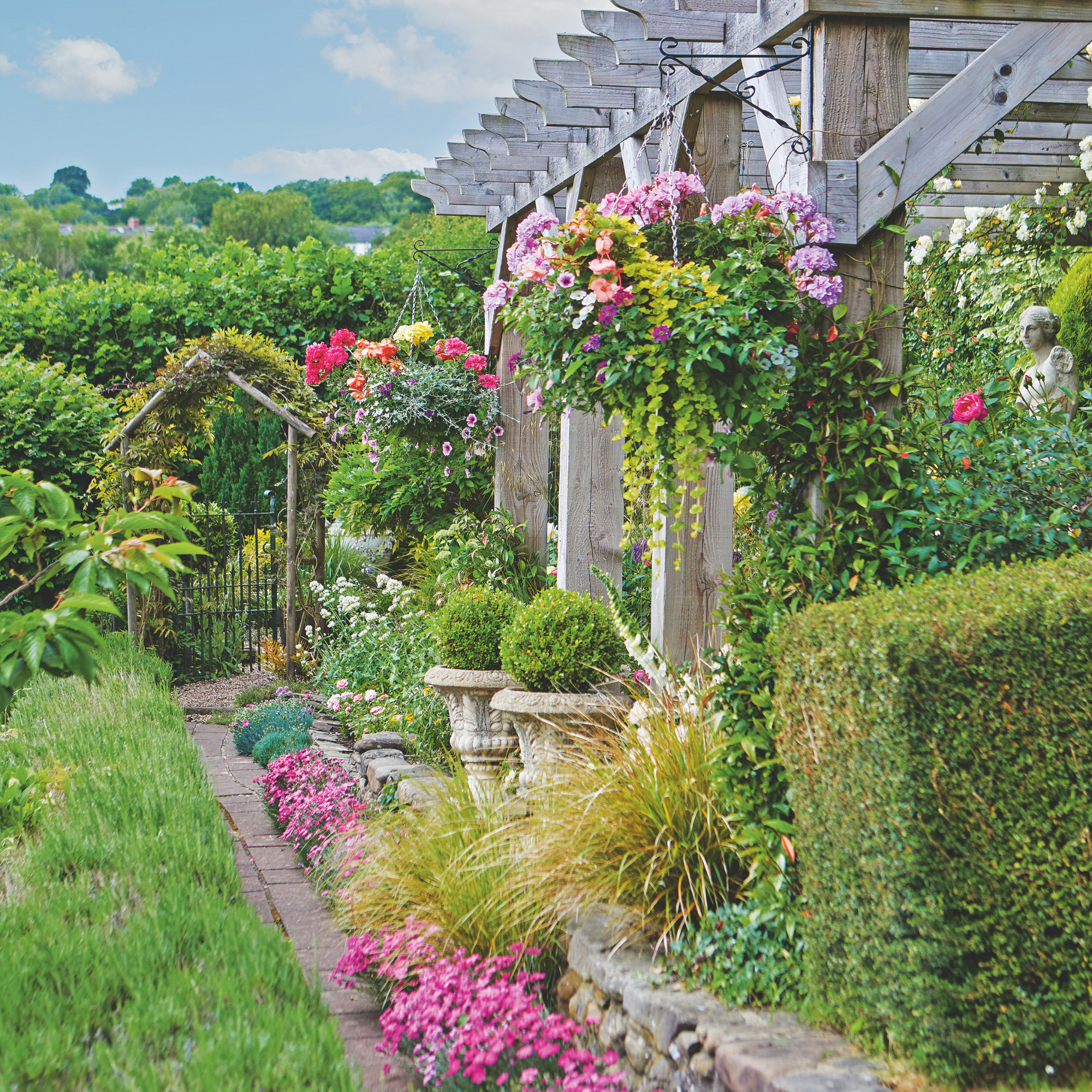 hedgrow lined with pots of bright pink flowers and hanging baskets.