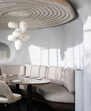 A futuristically designed restaurant features neutral colored furntirue in mid-century modern style including paper-like lighting pendants, curvilinear banquettes, and sculptural ceilings.