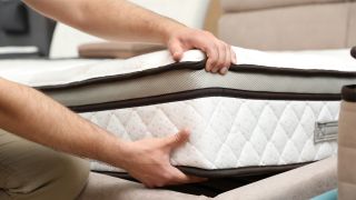 How to optimize your bedroom for sleep: A man checks over his mattress to ensure it's still comfy and clean